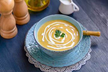 Creamy zucchini, yellow squash soup decorated with parsley and cream served in a blue bowl on dark wooden table. Top view, horizontal, selective focus