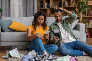 Upset african american family after tour cancellation sitting with travel tickets and unpacked suitcase