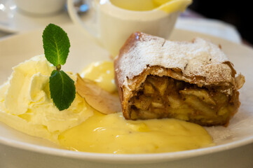 Austrian sweet dessert, portion of apple strudel with whippen cream and hot vanilla sauce served in old bakery cafe in Vienna, Austria