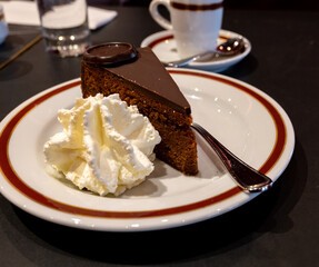 Piece of famous Sachertorte chocolate cake with apricot jam of Austrian origin served with whipped cream