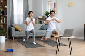Strong chinese spouses exercising together at home, watching fitness video