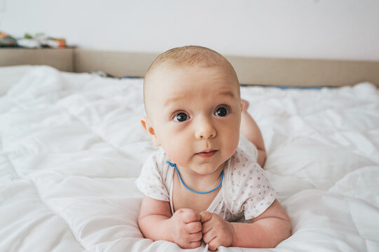 A small, smiling child, a boy, lies on a white bed and tries to crawl. 3, 4 months from the moment of birth. Photography, concept.
