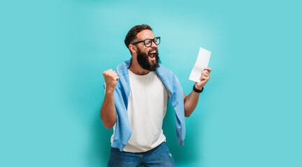 Excited happy young male winner feeling joy winning lottery, placing bets, getting cashback online gift isolated on blue background. Human face emotions and betting concept. Trendy colors - obrazy, fototapety, plakaty