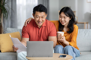 Smiling asian spouses paying bills online, using laptop