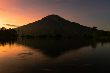 Sunrise with Mount Sumbing with lake surface on the foreground. The lake surface make reflection of mountain and sunrise sky. Embung Kledung, Central Java, Indonesia

