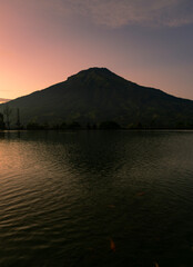 Sunrise with Mount Sumbing with lake surface on the foreground. The lake surface make reflection of mountain and sunrise sky. Embung Kledung, Central Java, Indonesia
