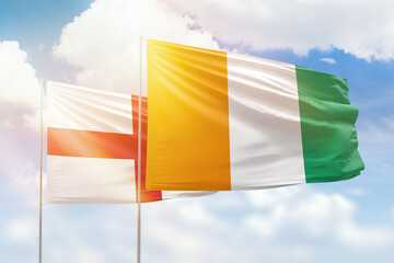 Sunny blue sky and flags of ivory coast and england