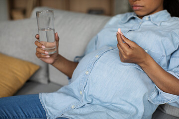 Unrecognizable Pregnant Black Woman Taking Pill Holding Glass At Home