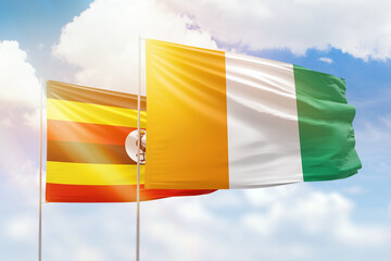 Sunny blue sky and flags of ivory coast and uganda