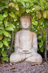Buda sculpture in lotus pose in the middle of some green leaves
