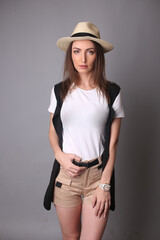 Portrait of a beautiful fashion girl brown-haired in the studio in a shorts and a t-shirt, in Hat