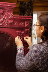 Old woman sticking carved from wood ornaments to wooden red cardboard color with round glass in...