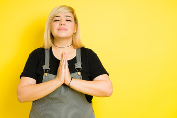 Pretty fat girl with her hands together and meditating in a studio with a yellow background