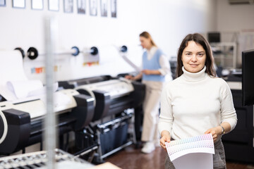 Portrait of positive woman printing office worker holding colour schedule and looking at camera.
