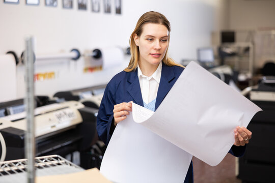 Woman checking large format paper after printing. Press worker looking at paper.