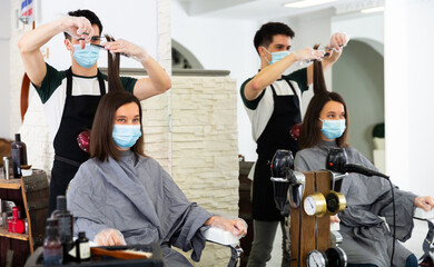 Fototapeta na wymiar Young man professional hairdresser in mask cut female's hair in hairdressing salon