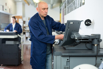 Man working in publishing facility, using printer, pushing buttons on display.