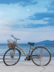 Fototapeta premium The bike is on the sandy beach. Against the background of the blue sky with the moon