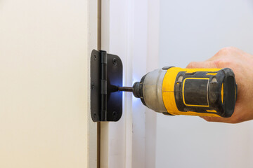 Installing the door hinge on the door frame using a screwdriver a new home - obrazy, fototapety, plakaty