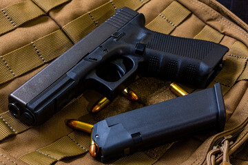 Artistic photo of a semi automatic 9mm handgun on a brown background in a tactical military setting with a loaded magazine and loose rounds of ammunition