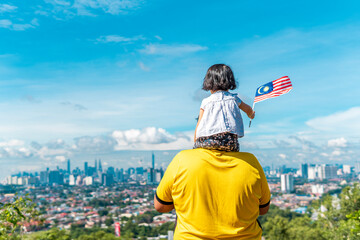 Local father and daughter holding a Malaysian flag at the top of a hill. All over Malaysia will be flagged for the celebration of independence day in month of august. - 510734995