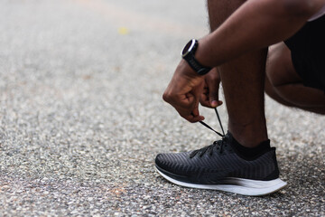Close up Asian sport runner black man wear watch sitting he trying shoelace running shoes getting...