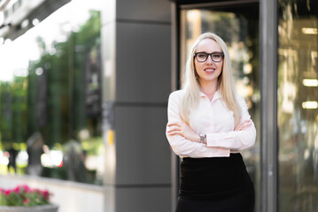 Beautiful business lady in a shirt, black skirt and glasses posing. Smiling and looking at the camera in front of the entrance to the business center