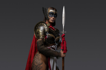 Portrait of seductive amazon from past with painted face and red cloak holding spear. - obrazy, fototapety, plakaty