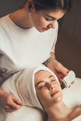 Fototapeta na wymiar Beautiful woman receiving ultrasonic skin cleansing procedure. Ultrasonic cleaning procedure. Hardware cosmetology.