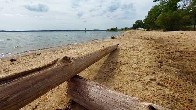 Deserted beachfront at the at Ebenezer Church Day-Use Area of Jordan Lake State Recreation Area. Dramatic clouds and driftwood in the foreground. Clean sand, no trash. Gentle waves lapping the shore.