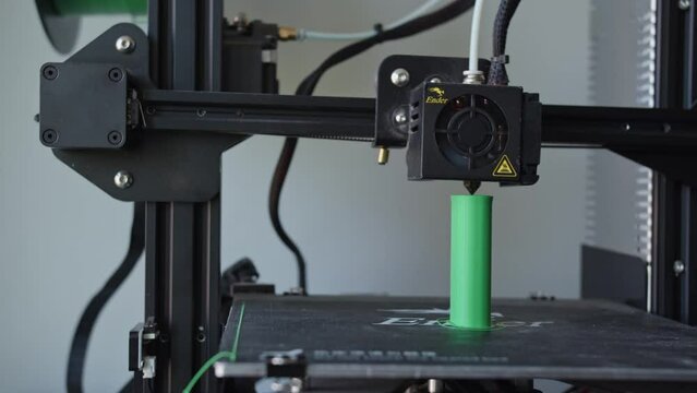 Black 3D Printer Printing a Small Green Plastic Element