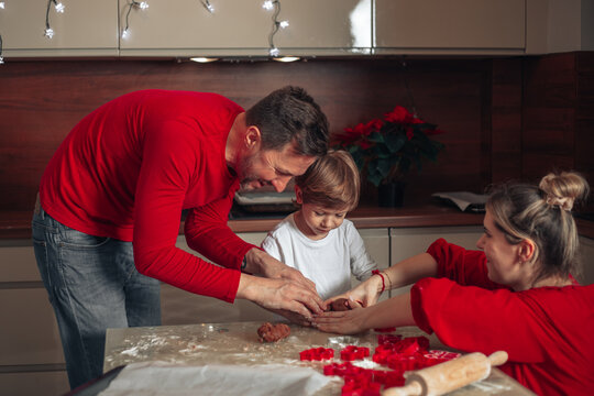Family is real team, Christmas cookies are baking, dad, mom and child are happy to spend time together. People have fun, dressed in red clothes. - Powered by Adobe