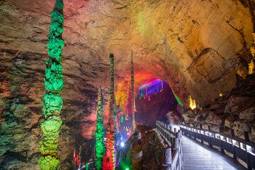 The passage through Huanglong limestone cave with stalactites and stalagmites with colorful lighting, horizontal image with copy space, wallpaper, background