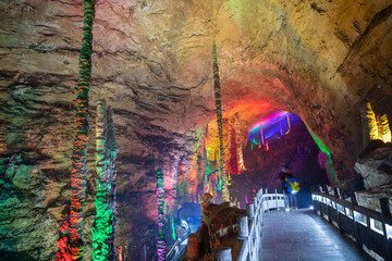 The person going through the passage of Huanglong limestone cave with stalactites and stalagmites with colorful lighting, horizontal background image with copy space for text
