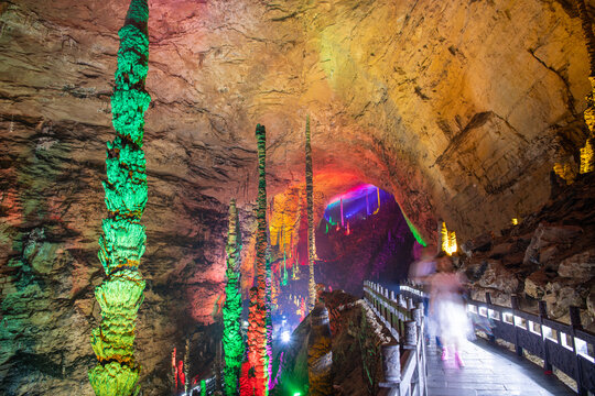 Horizontal image of the passage through Huanglong limestone cave with stalactites and stalagmites with colorful lighting, yellow, green, purple and blue colors