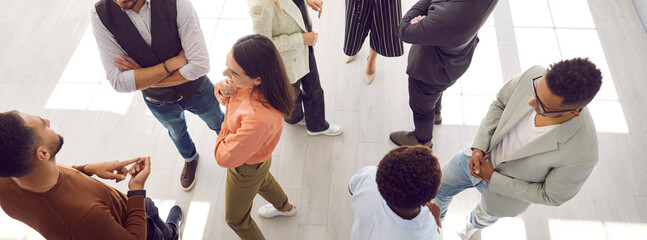 Young people meeting, interacting and making contacts at business event session. Group of multi ethnic participants standing in office and talking. High angle, overhead top view, above. Header, banner - obrazy, fototapety, plakaty