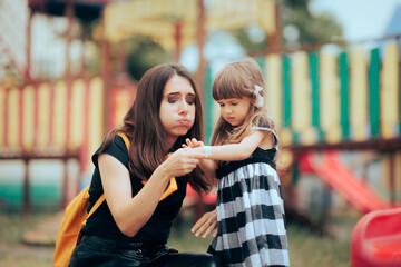 Mom Applying a Plaster on an Injured Daughter at the Playground. Sad wounded child receiving first...