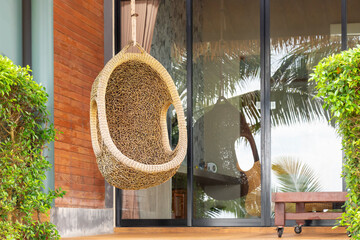 A wicker armchair in the form of a cocoon suspended on the terrace. The recreation scene, the...
