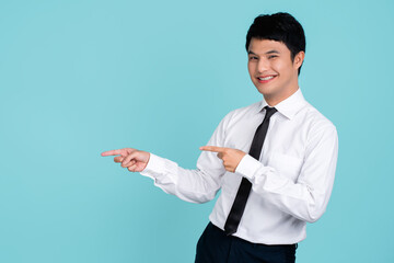 Check it. Portrait of young smiling asian man standing on light blue isolated background and pointing with his index fingers aside.