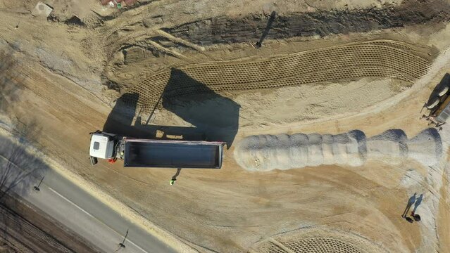 Above top view, overhead on tipper truck as lifting his trailer to unload cargo, fraction, small crushed stone for new circular road, roundabout under construction.