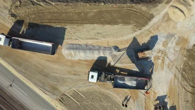 Above top view, overhead on tipper truck as lifting his trailer to unload cargo, fraction, small crushed stone that bulldozer crawler is pushing, leveling at construction site.