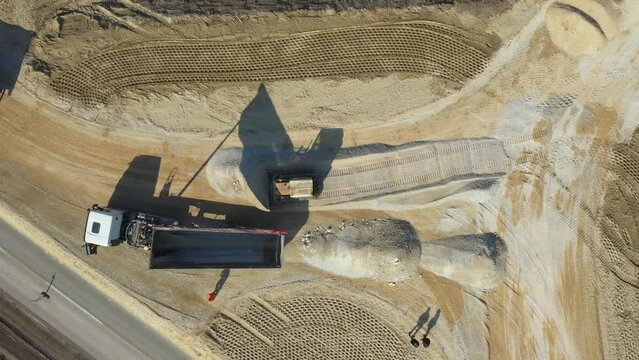 Above top view, overhead on tipper truck as lifting his trailer to unload cargo, fraction, small crushed stone that bulldozer crawler is pushing, leveling at construction site.