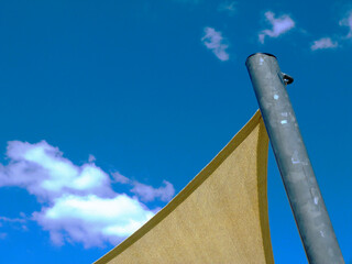 fabric sun shade material spanning over terrace or patio area. blue sky and white clouds. Loosely...