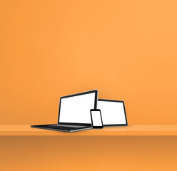 Laptop, mobile phone and digital tablet pc on orange wall shelf. Square background