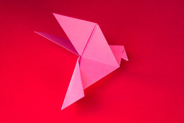 Pink paper dove origami isolated on a red background