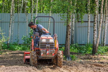 A farmer on a mini tractor loosens the soil for the lawn. Land cultivation, surface leveling.