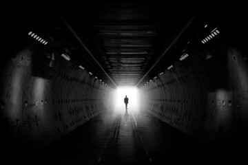 Dreaming, man in dark tunnel. Freedom light in tunnel. Silhouetted desaturated. Silhouette of a woman walking into the light. Light at the end of the tunnel. business man in silhouette walking