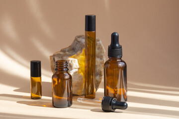 Empty brown amber glass bottles with open and closed dropper lids for cosmetics, oils, serums in sunlight on beige background. Close-up, mockup