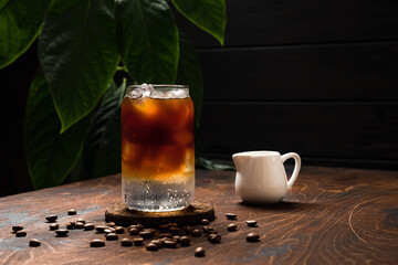 Cold espresso tonic. A highball glass filled with ice cubes, tonic soda water, coffee beans around, milk jug, wooden background - 510759324
