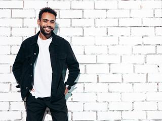 Handsome smiling hipster model. Sexy unshaven man dressed in black  summer shirt and jeans clothes. Fashion male posing near white brick wall in studio at sunny day. Isolated